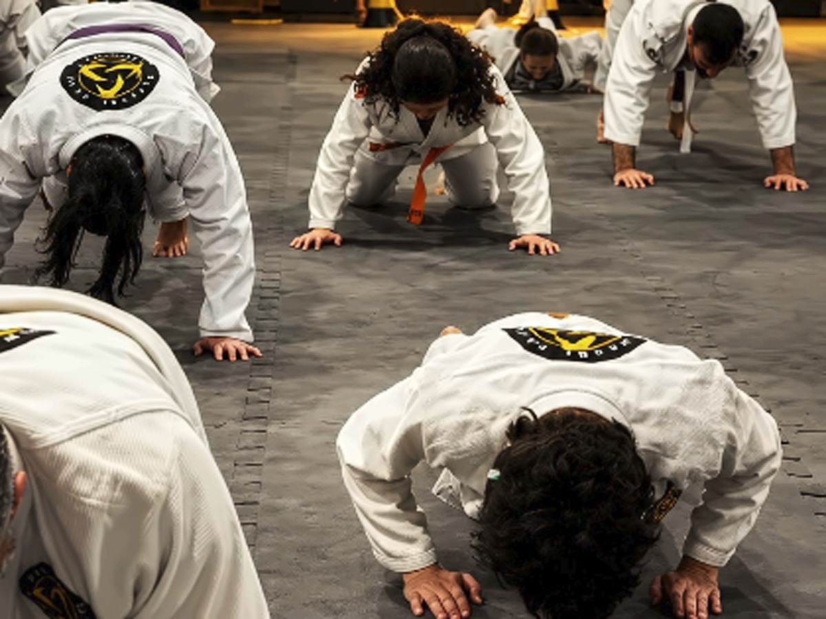 Crianças e adultos fazendo flexões no dojô